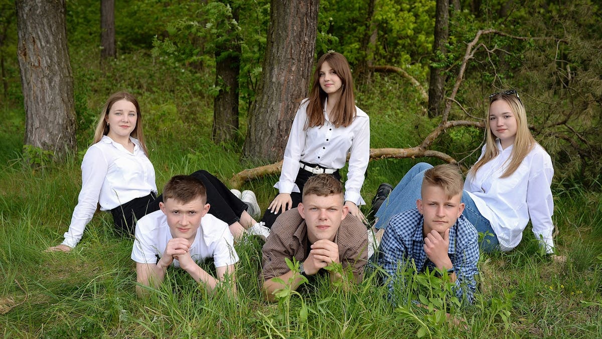 A group of young adults posing together on grass in a forest setting.